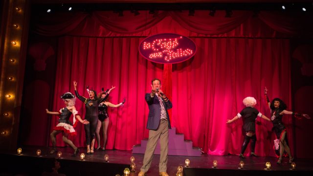 Georges (Ryan Drummond*) announces the night's entertainment at La Cage aux Folles.