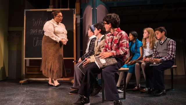 Miss Shields (Katrina Lauren McGraw) collects her students' papers.