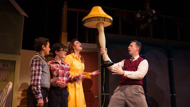 The Old Man (Ryan Drummond*, right) unveils his major award as Randy (Jake Miller), Ralphie (Jonah Broscow*), and Mother (Abby Haug*) express their puzzlement.