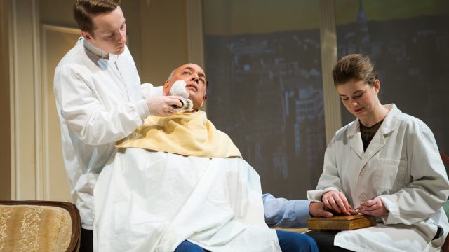 A Barber (Casey Robert Spiegel) shaves Harry Brock as a Manicurist (Melissa Quine) touches up his fingernails.