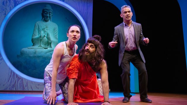 Romola (Ayelet Firstenberg*) tries to teach Gururaj (Bobak Cyrus Bakhtiari*) yoga with the help of Fred (Ryan Morales).