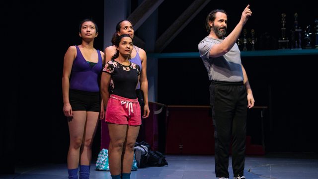 Zuzu (Krystle Piamonte), Connie (Mohana Rajagopal), and Ashlee (Lauren Spencer) look on as Dance Teacher Pat (Liam Robertson) explains their next performance.