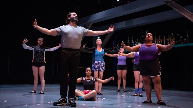 Dance Teacher Pat (Liam Robertson) leads the dance team (Ash Malloy, Mohana Rajagopal, Julia Brothers, Lauren Spencer, Indiia Wilmott) in warm-up exercises.