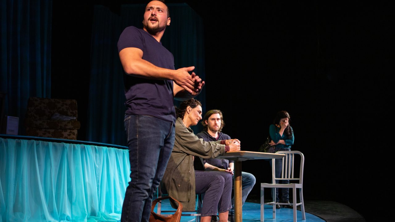 Elliot Ortiz (Xander DeAngeles*) arrives at a meeting between his mother Odessa Ortiz (Lisa Ramirez*) and Fountainhead (Ben Euphrat*) as Yazmin Ortiz (Lara Maria*) looks on.