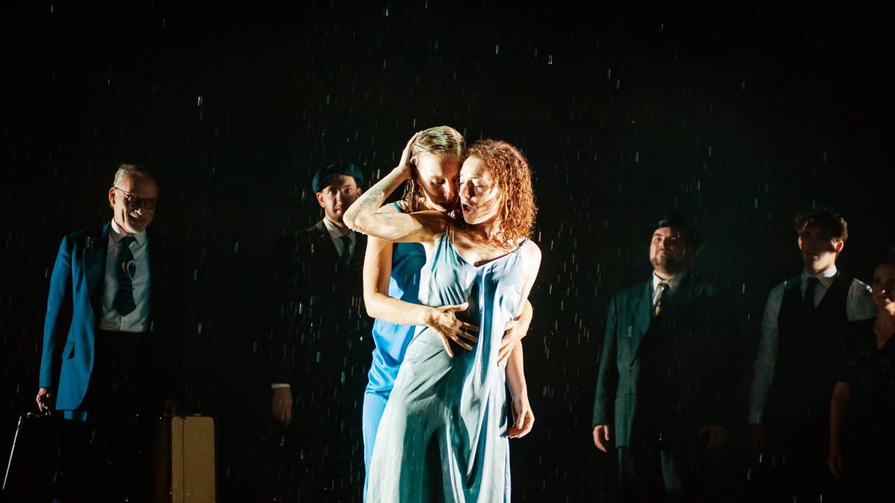 Halina as Manke (Rivka Borek*, left) and Chana as Rifkele (Malka Wallick*, right) and embrace each other in the rain in the legendary "rain scene" of Sholem Asch's 'The God of Vengeance', the play within the play, as the rest of the troupe looks on (background, L-R): Otto (Victor Talmadge*), Lemml (Dean Linnard*), Mendel (Ted Zoldan), Avram (Billy Cohen*), and Vera (Rachel Botchan*). Production photography by Jessica Palopoli for 'Indecent' by Paula Vogel at San Francisco Playhouse.