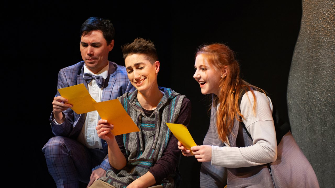 Touchstone (Nicholas Yenson), Rosalind (River Navaille) disguised as Ganymede, and Celia (Abigail Esfira Campbell) disguised as Aliena read Orlando's love notes in San Francisco Playhouse's musical version of "As You Like It," performing now through January 14, 2023.
