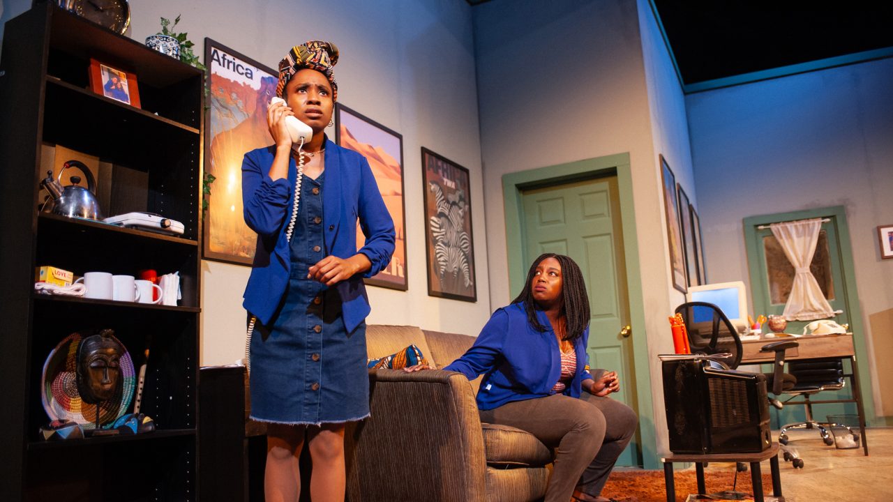 Ayamma (Angel Adedokun) receives a call while working with her sister Dede (Brittany Nicole Sims) at their parents' travel agency in San Francisco Playhouse's "Nollywood Dreams," performing September 28 - November 4, 2023.