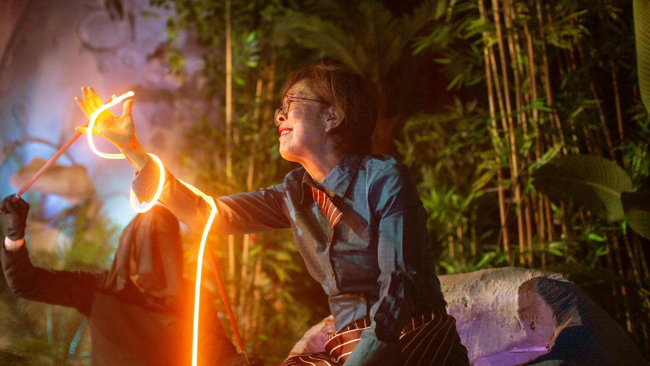 Lan (Sharon Omi) reminisces about her childhood with a giant noodle (background: puppeteered by Erin Mei-Ling Stuart) on the moon in San Francisco Playhouse's World Premiere Play "My Home on the Moon," performing January 25 - February 24.