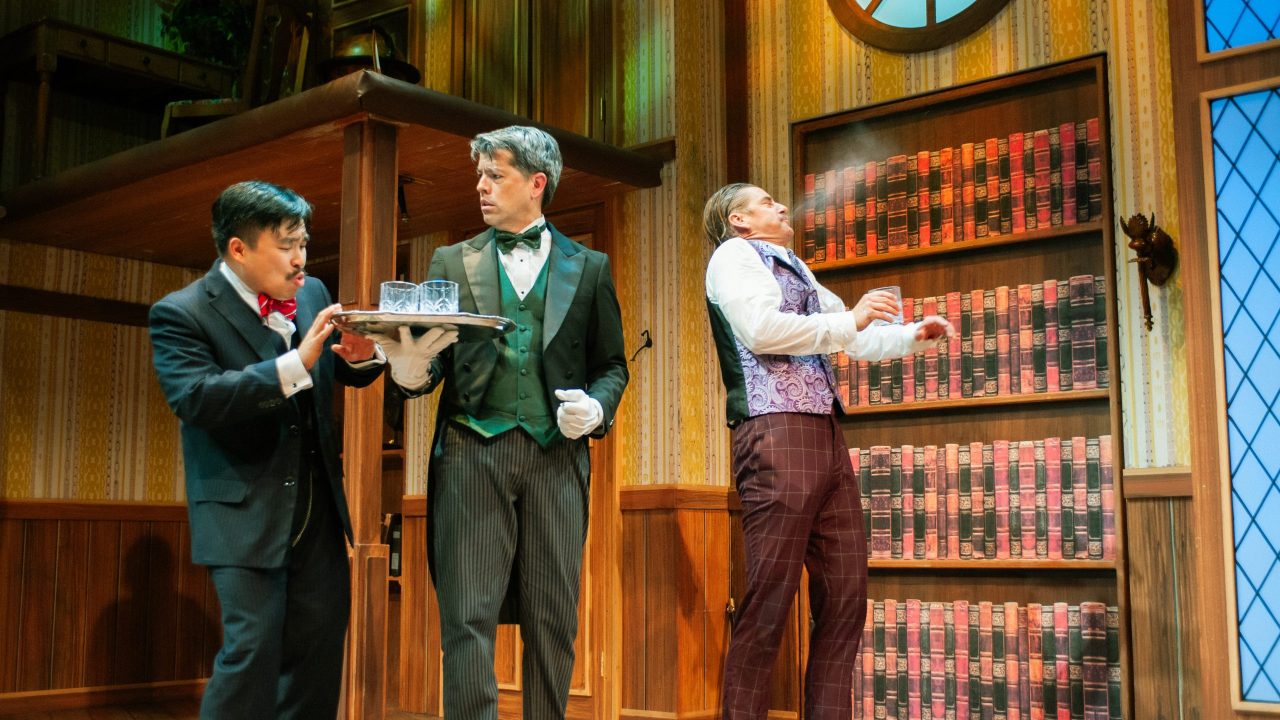 Chris (Phil Wong) declines a drink from Dennis (Greg Ayers) as Robert (Patrick Russell) does a spit take in "The Play That Goes Wrong," presented by San Francisco Playhouse September 21 - November 9. "The Play That Goes Wrong" production photo.